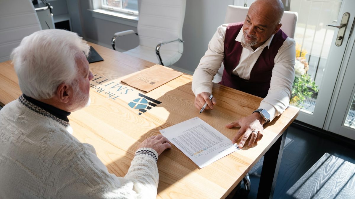 Two men discuss financial documents at a wooden table, highlighting the impact of financial stress on men's health.