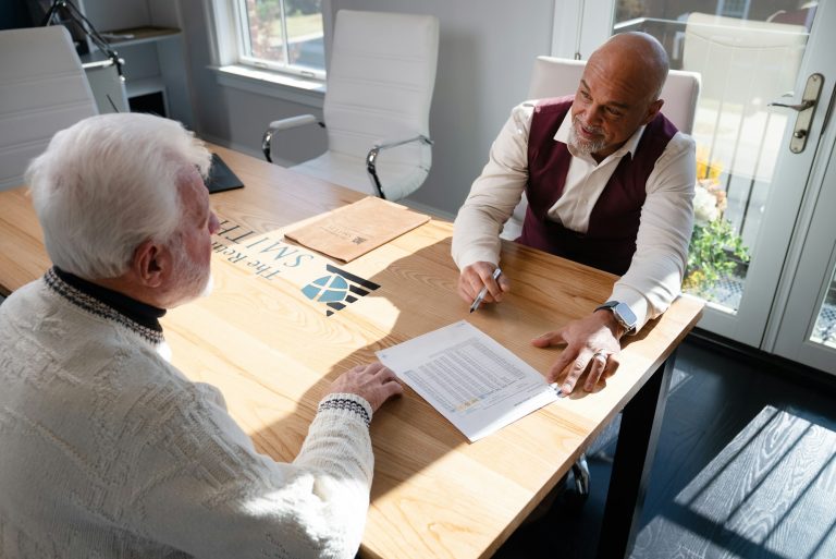 Two men discuss financial documents at a wooden table, highlighting the impact of financial stress on men's health.