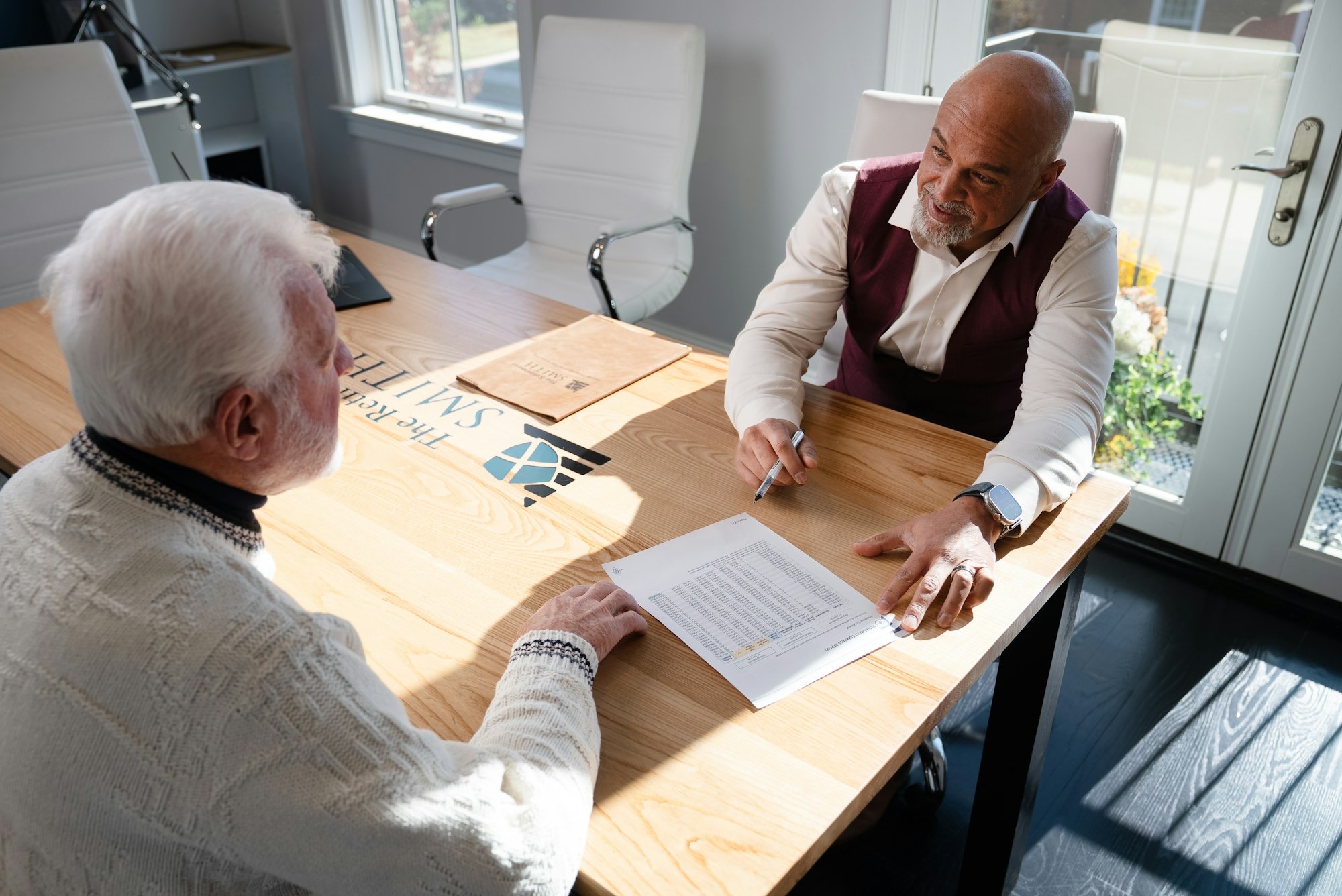 Two men discuss financial documents at a wooden table, highlighting the impact of financial stress on men's health.