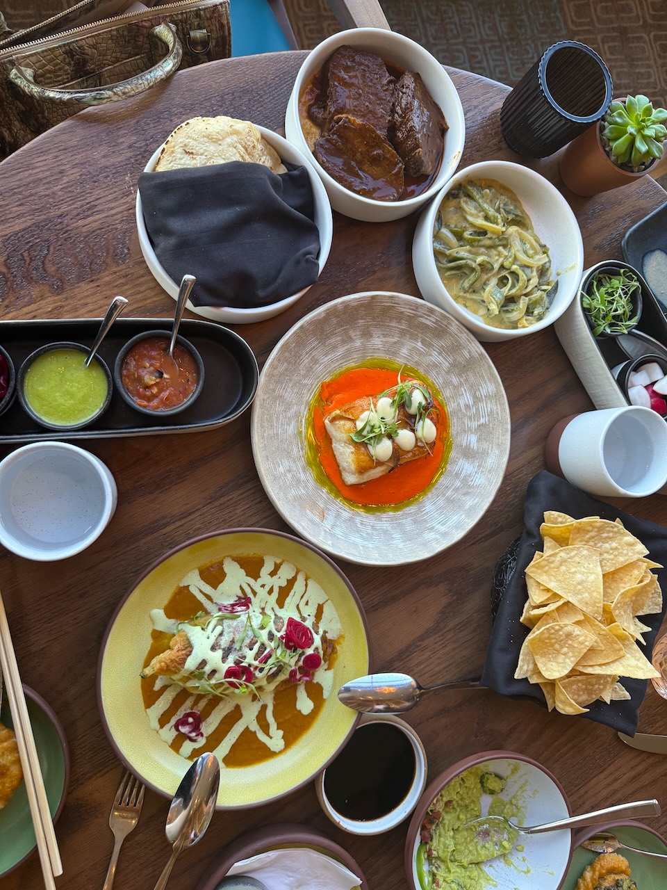 A variety of dishes including fish, beef, sauces, and chips served on a wooden table, showcasing Nikkei flavors.