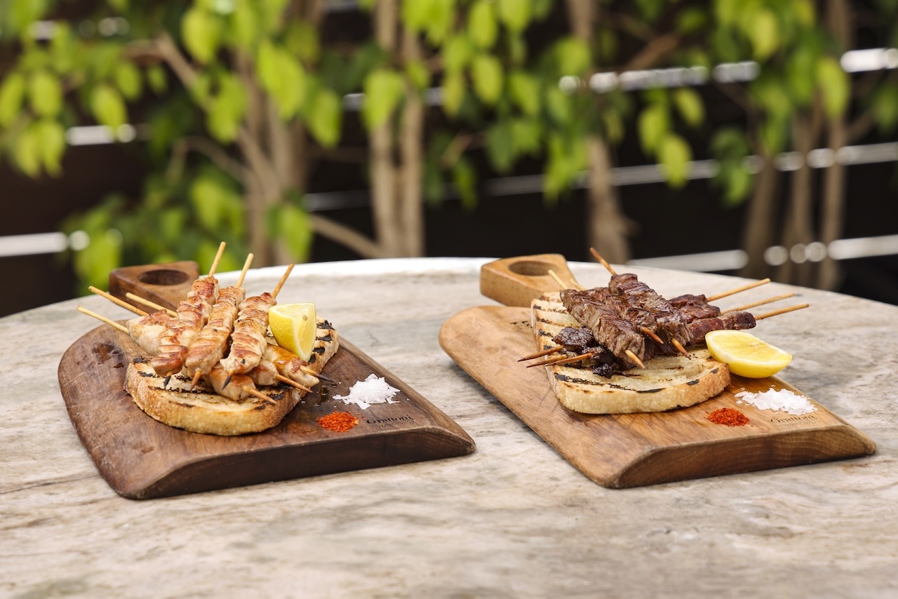 Grilled arrosticini skewers served on wooden boards with lemon wedges and seasonings, set against a green backdrop.