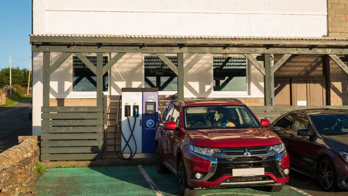 Red electric vehicle parked near a charging station outside a building, illustrating modern charging habits for staycations.