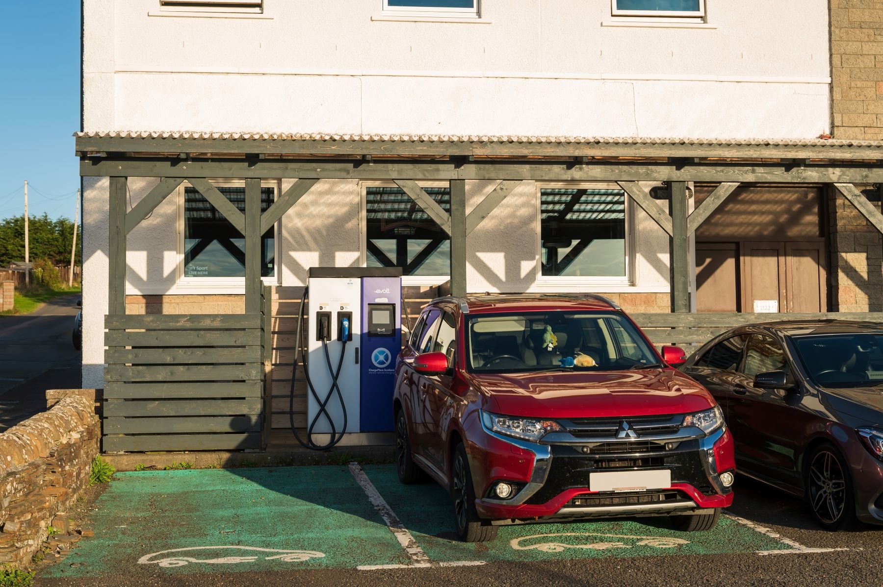 Red electric vehicle parked near a charging station outside a building, illustrating modern charging habits for staycations.
