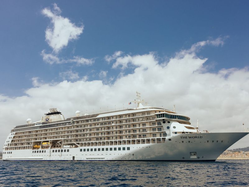 Luxury cruise ship The World anchored in calm waters under a blue sky with clouds.