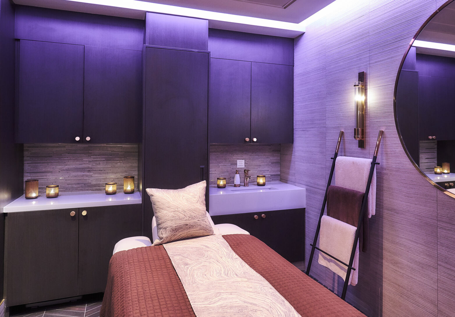 A serene spa room featuring soft lighting, a massage table, and neatly arranged towels, creating a tranquil ambiance.