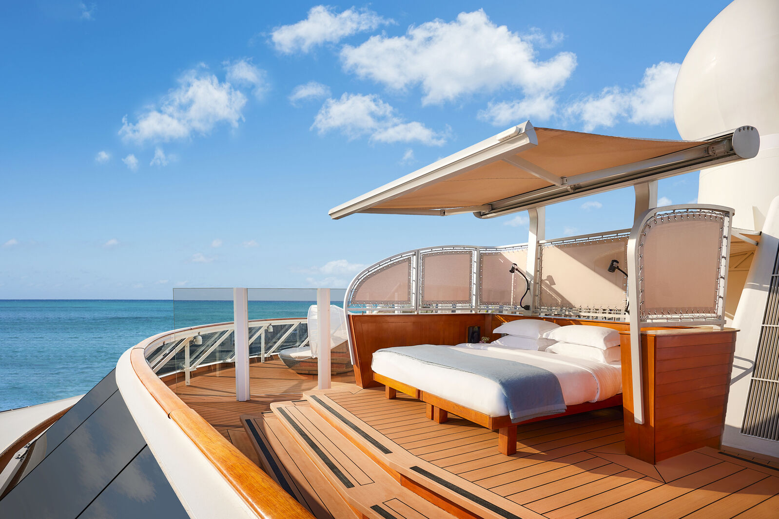 A luxurious outdoor bed on a private luxury ship, overlooking the ocean with a clear blue sky and comfortable seating.