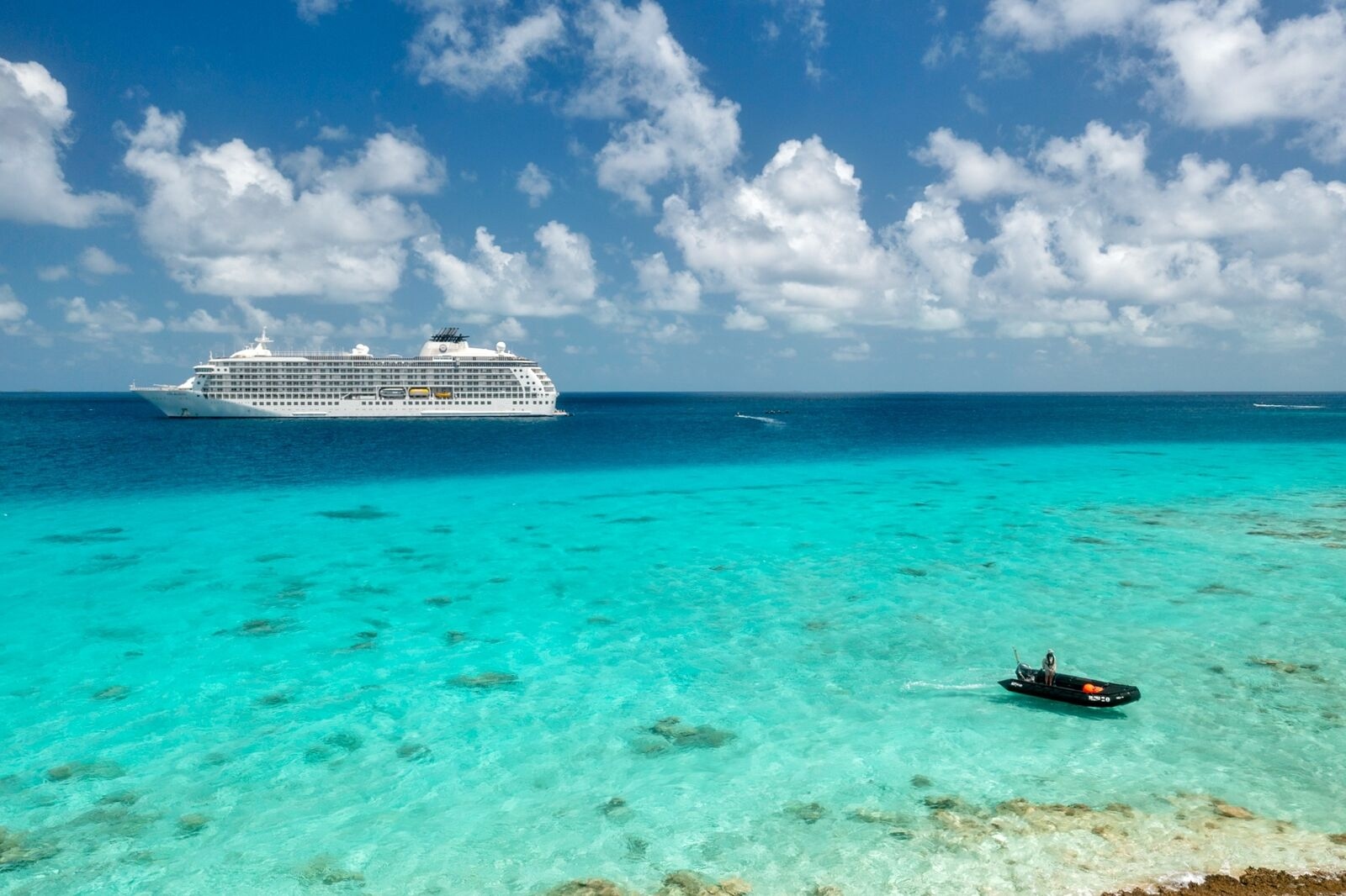 Luxury ship anchored in turquoise waters, with a small boat nearby under a clear blue sky.