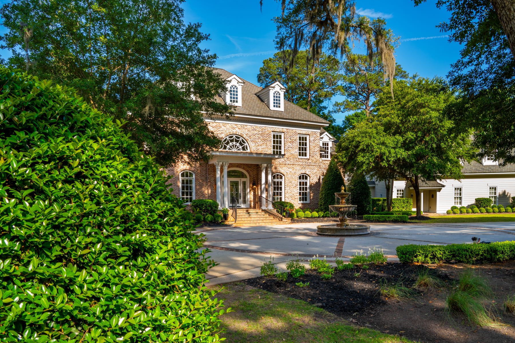 Luxurious brick home with a fountain, surrounded by lush greenery in the Colleton River Estate, Bluffton.
