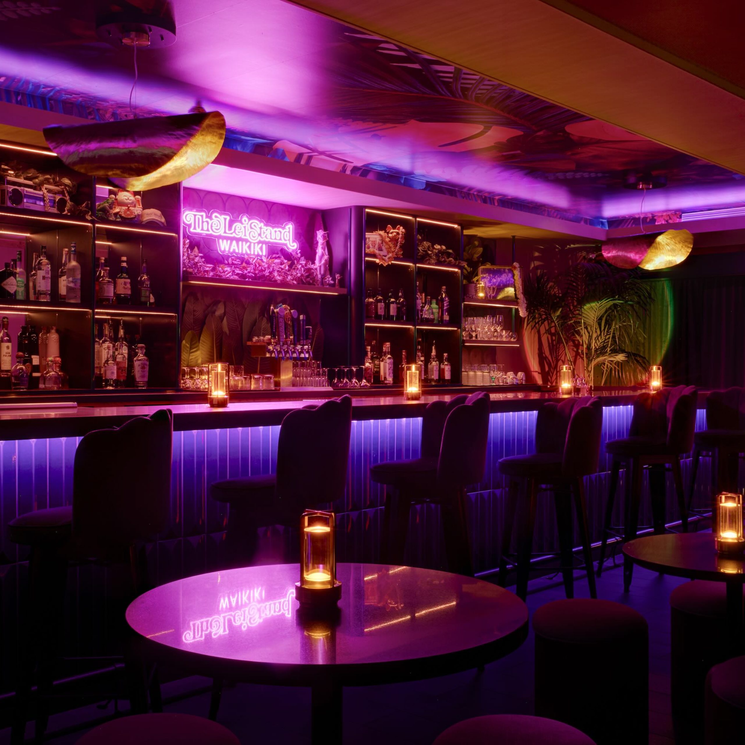 Vibrant interior of The Lei Stand bar in Waikīkī, featuring colorful lighting, a well-stocked bar, and cozy seating.