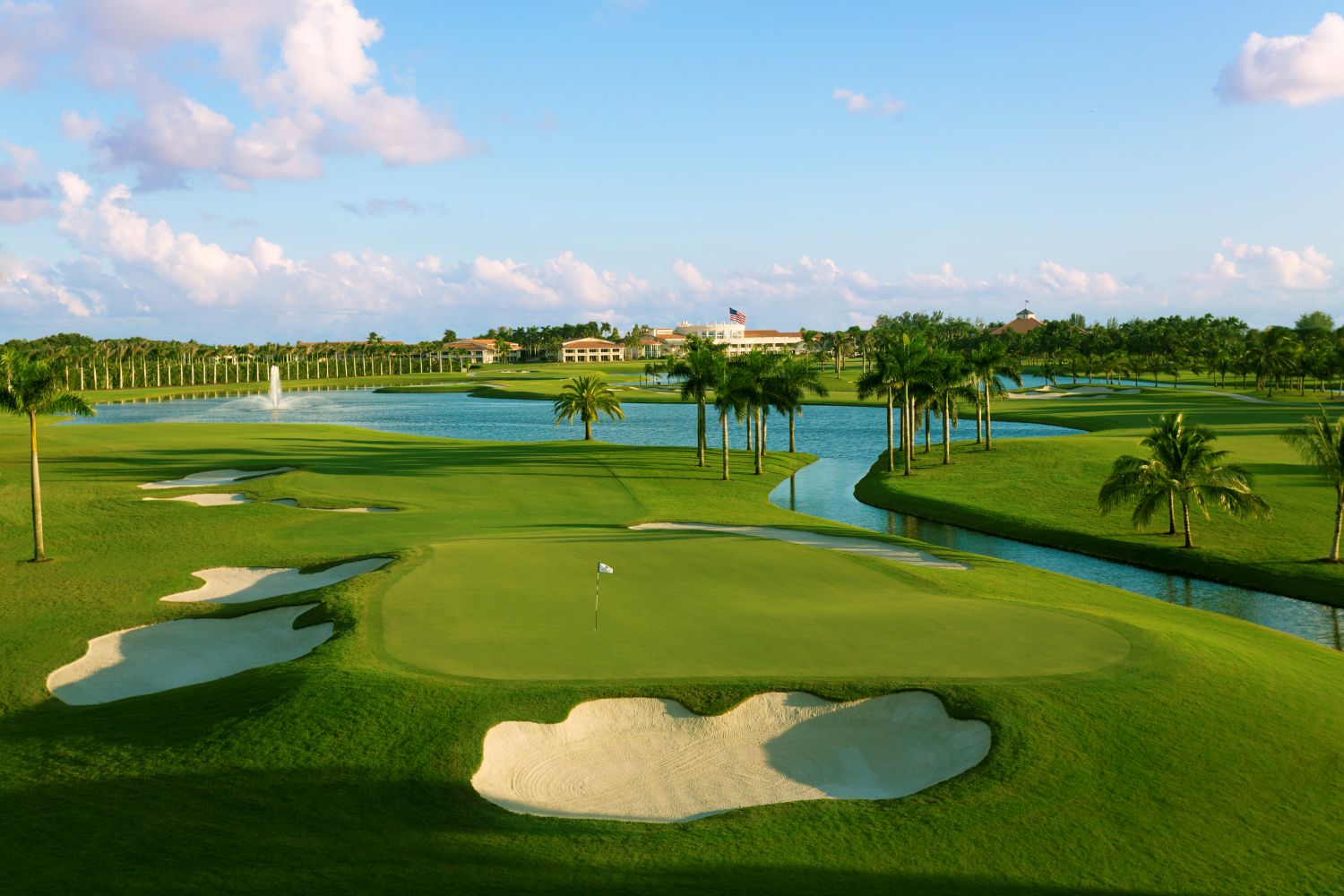Lush green golf course with a waterway, sand traps, and palm trees, set against a vibrant sky at a luxury resort in South Florida.