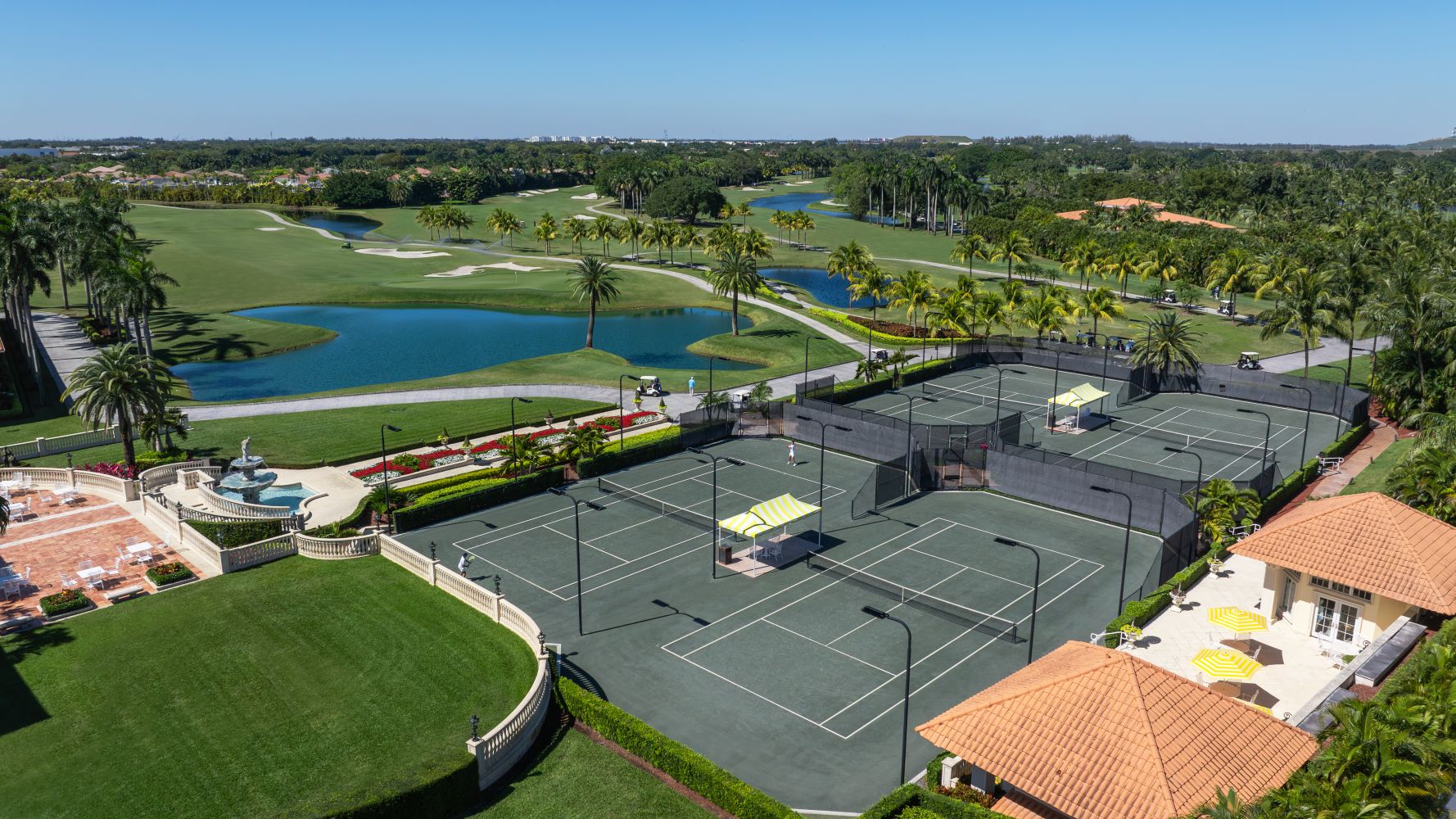 Aerial view of tennis courts surrounded by lush landscaping and serene water features at a luxurious South Florida resort.