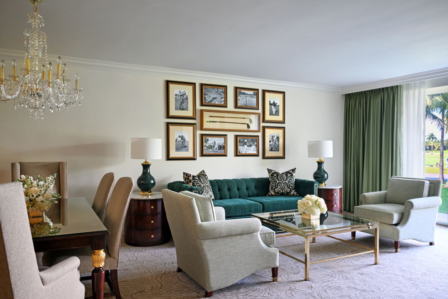 Luxurious guest room featuring a teal sofa, elegant chandelier, framed artwork, and a view of palm trees through large windows.