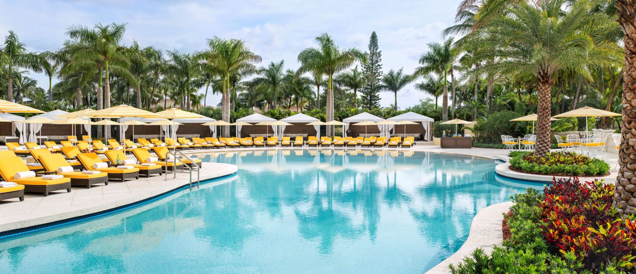 Luxurious pool area with yellow lounge chairs and umbrellas, surrounded by palm trees at a South Florida resort.