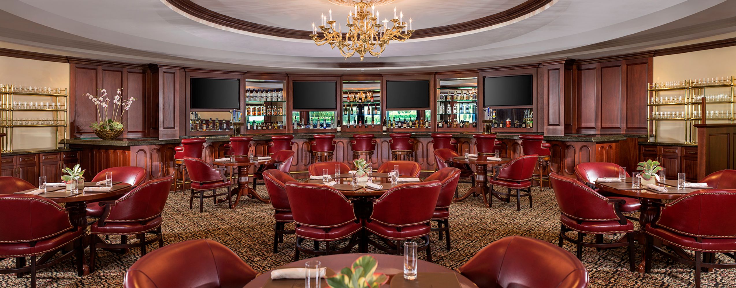 Elegant bar area featuring rich wooden furnishings, plush red seating, and a chandelier, ideal for dining and relaxation.