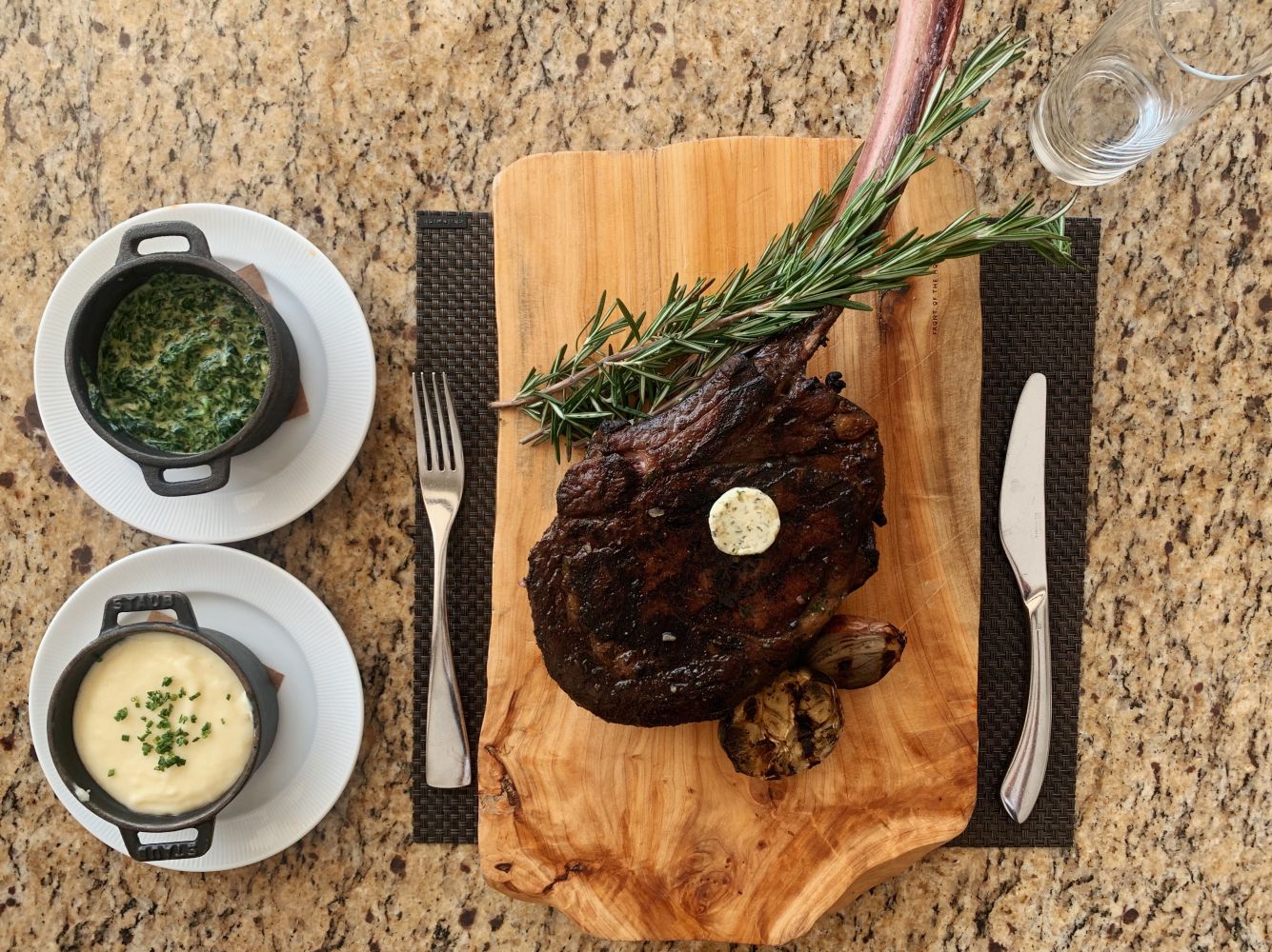 A beautifully plated gourmet steak with rosemary, accompanied by creamy mashed potatoes and sautéed spinach.