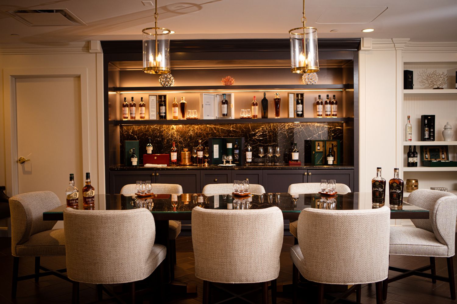 Elegant salon with a bar, featuring a variety of spirits, surrounded by plush seating and stylish lighting.