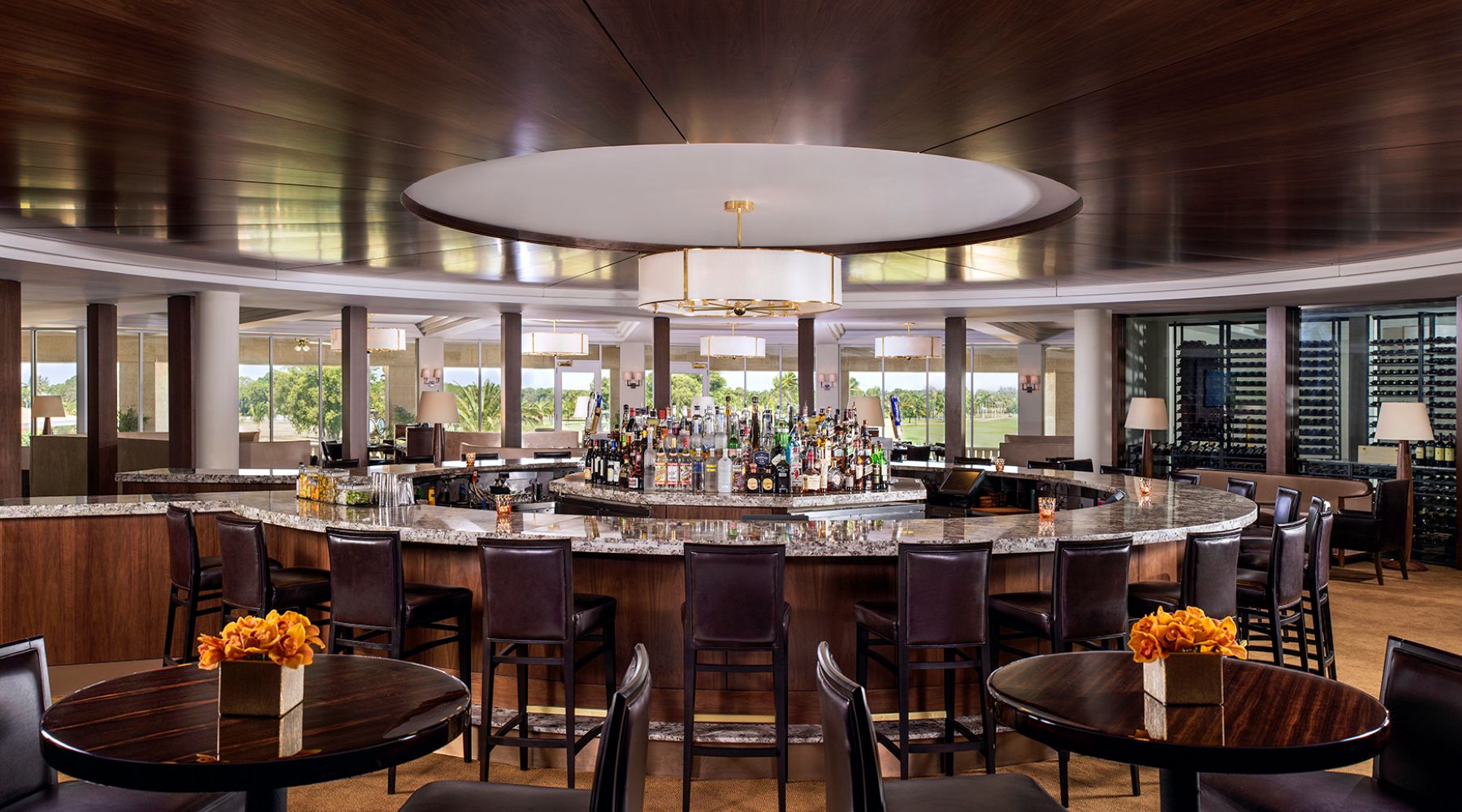 Luxurious bar area featuring a curved marble counter, high chairs, and a variety of spirits, set in an elegant South Florida resort.