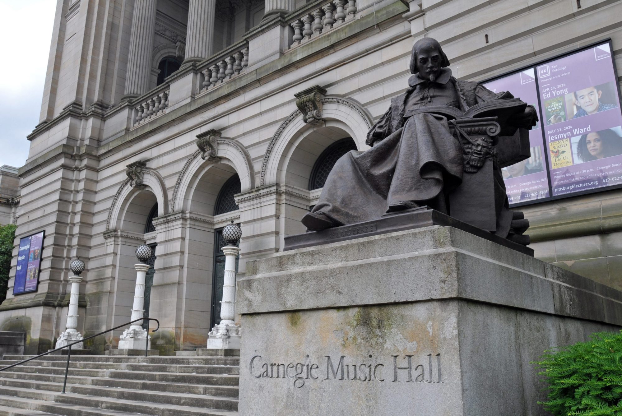 Statue of Shakespeare seated outside Carnegie Music Hall with its architectural details and promotional posters in view.