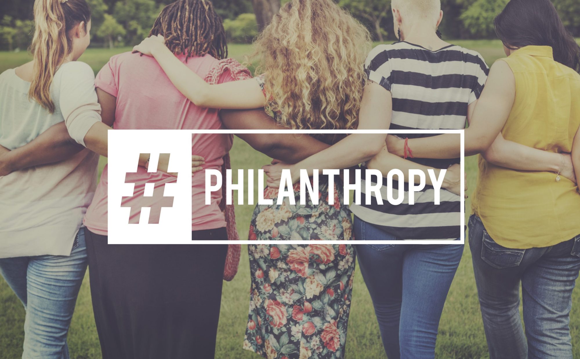 Women standing together with arms around each other, showcasing a sense of community and philanthropy in a green outdoor setting.