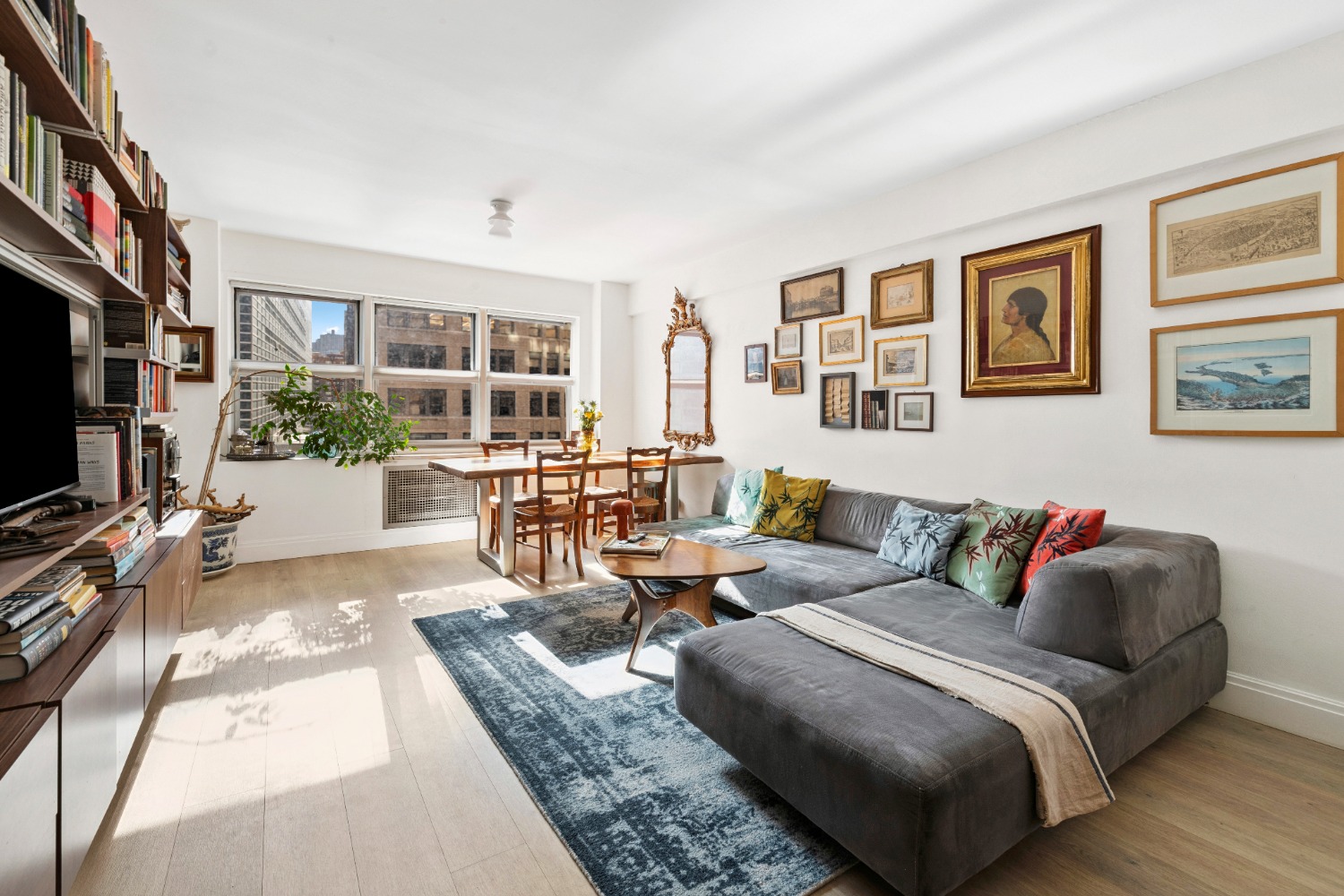 Spacious living area featuring a gray sectional sofa, dining table, wall art, and large windows with city views.