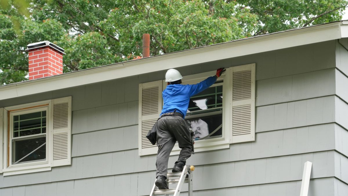 A worker installs new home windows while on a ladder, showcasing the window replacement process in a residential setting.