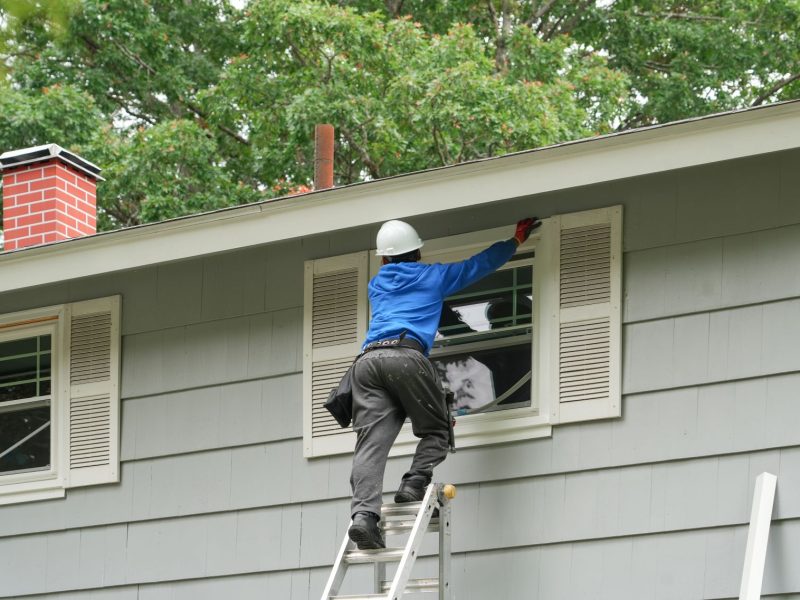 A worker installs new home windows while on a ladder, showcasing the window replacement process in a residential setting.