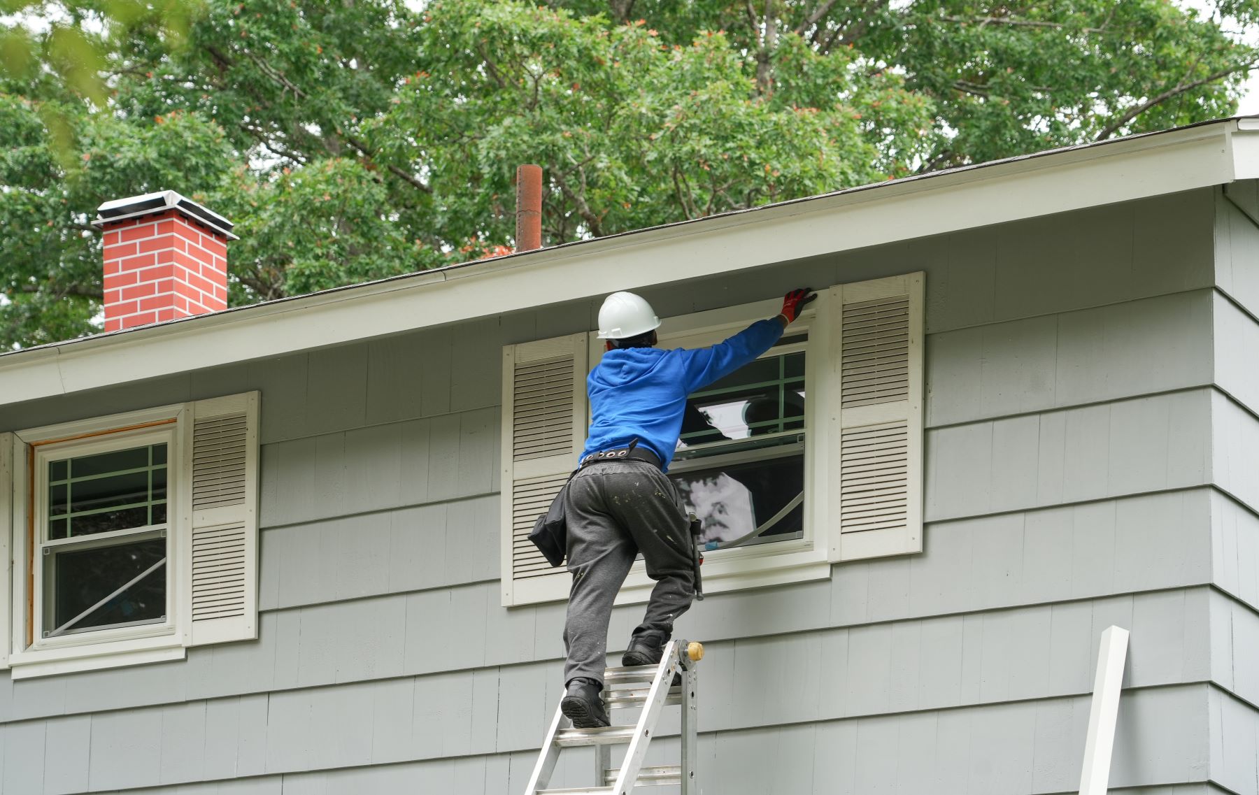 A worker installs new home windows while on a ladder, showcasing the window replacement process in a residential setting.