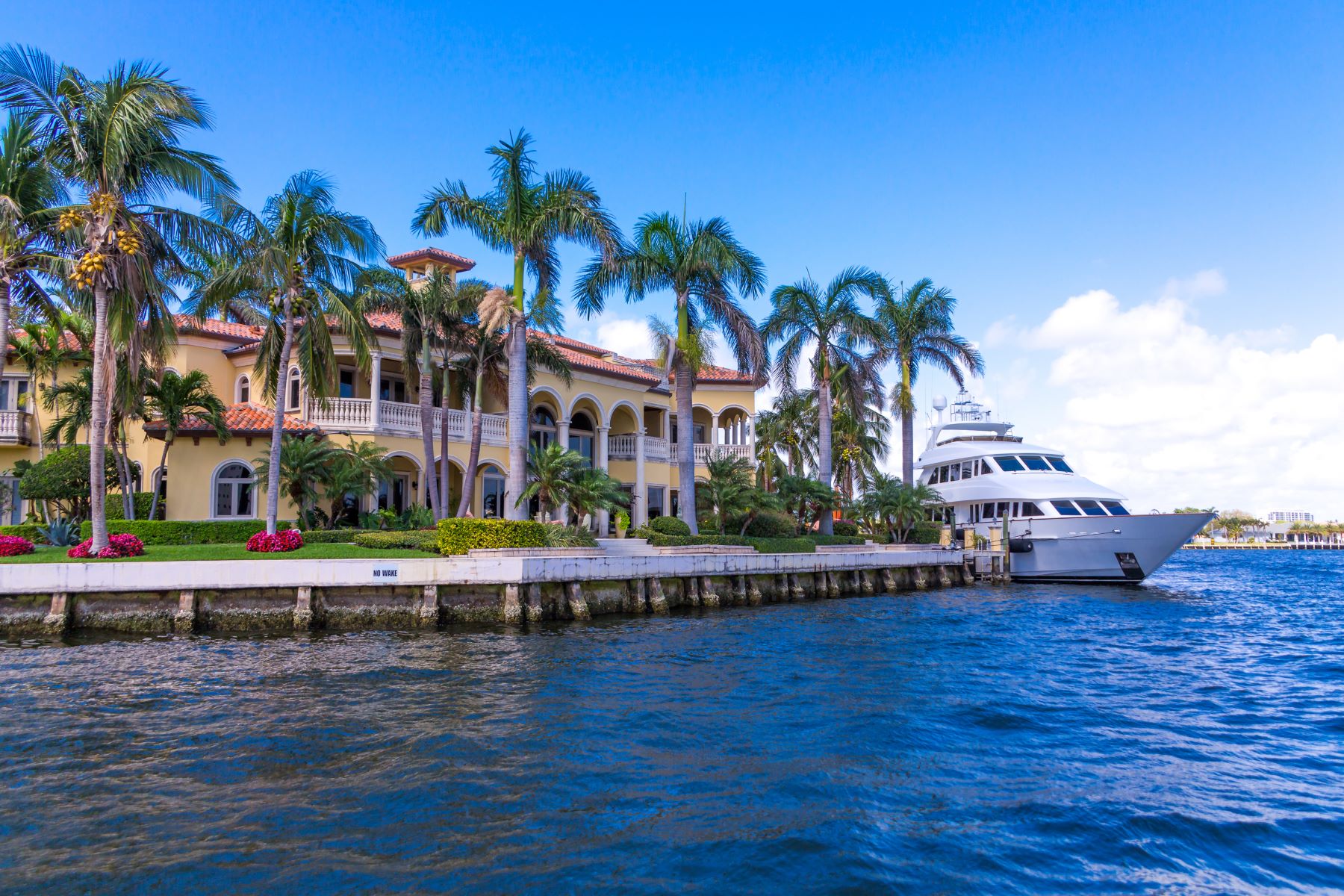 Luxury waterfront property with palm trees and a yacht docked nearby, showcasing an upscale real estate market.