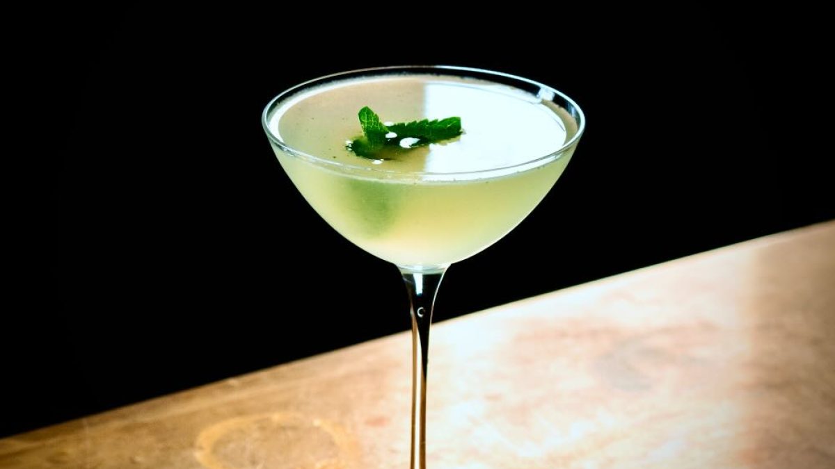 A South Side cocktail featuring a green mint garnish in a stylish glass on a wooden surface.