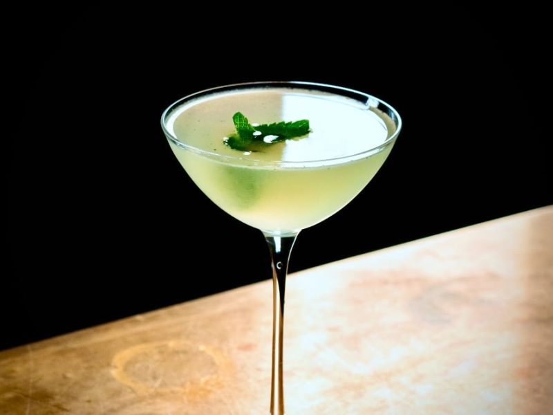A South Side cocktail featuring a green mint garnish in a stylish glass on a wooden surface.