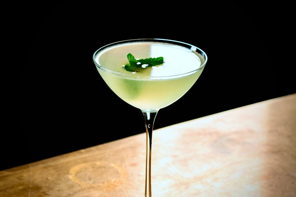 A South Side cocktail featuring a green mint garnish in a stylish glass on a wooden surface.