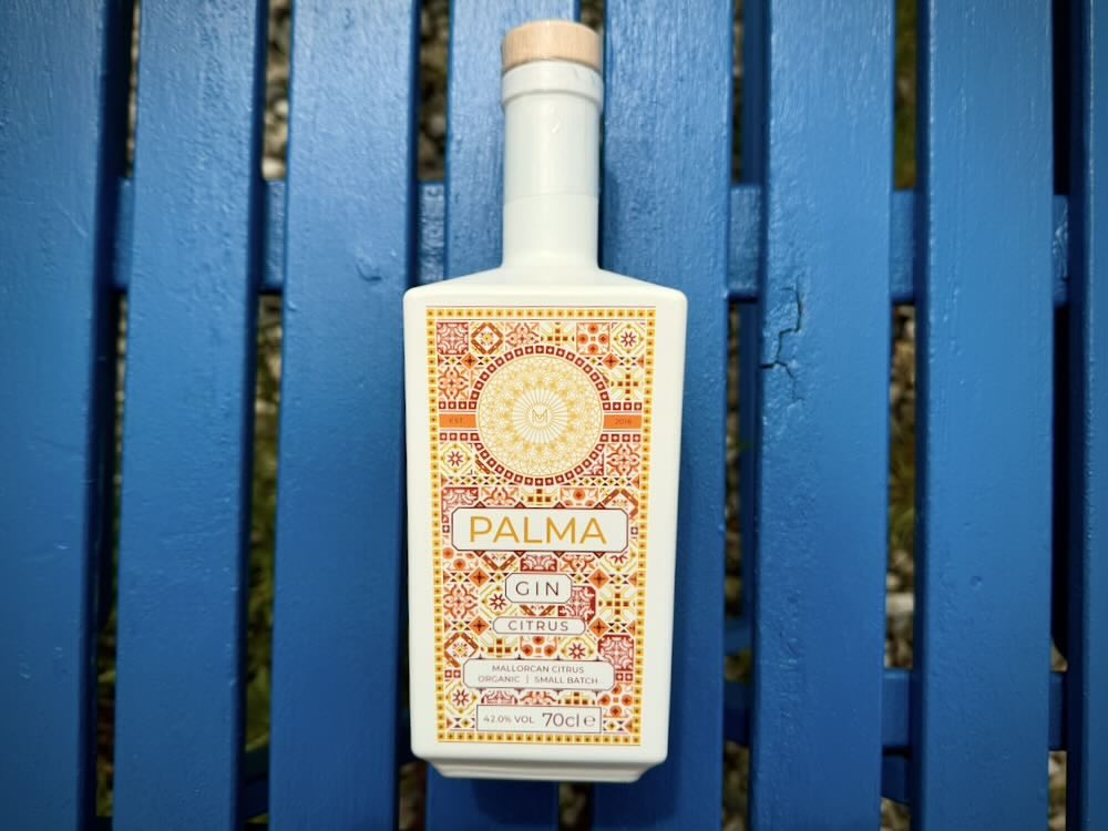 Palma gin bottle with a colorful label featuring citrus motifs, placed on a blue wooden surface.