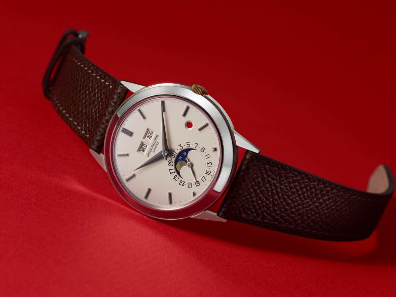Patek Philippe watch featuring a silver dial with date and moon phase display, set on a dark brown leather strap.