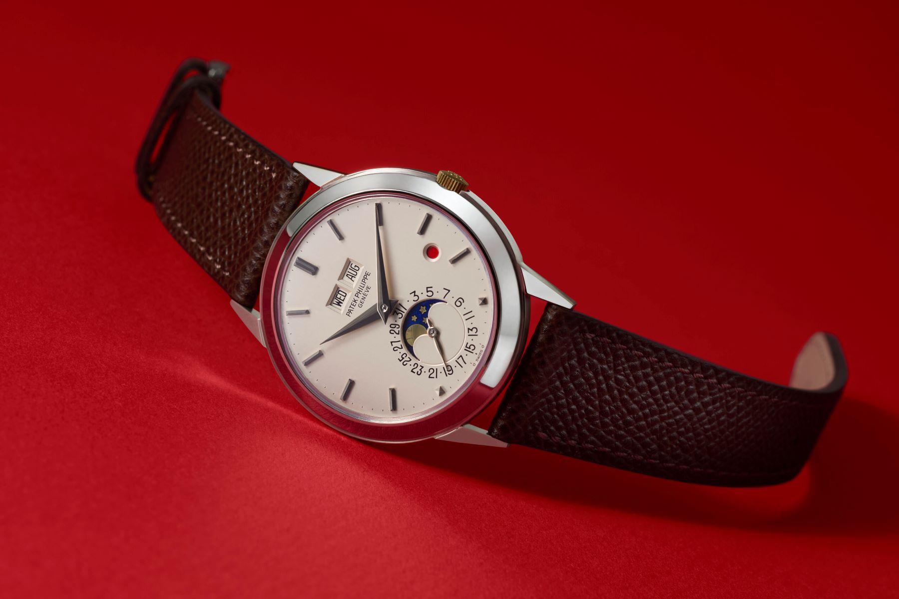 Patek Philippe watch featuring a silver dial with date and moon phase display, set on a dark brown leather strap.