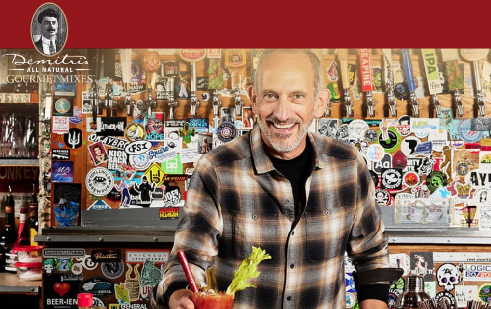 Entrepreneur holding a Bloody Mary, smiling in front of a bar adorned with stickers and beer taps.