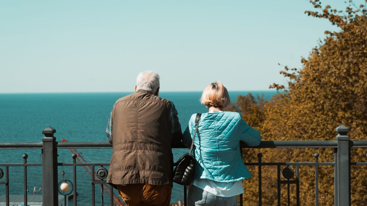 An older couple enjoys a serene view of the ocean while leaning on a railing, highlighting the importance of comfort in travel.