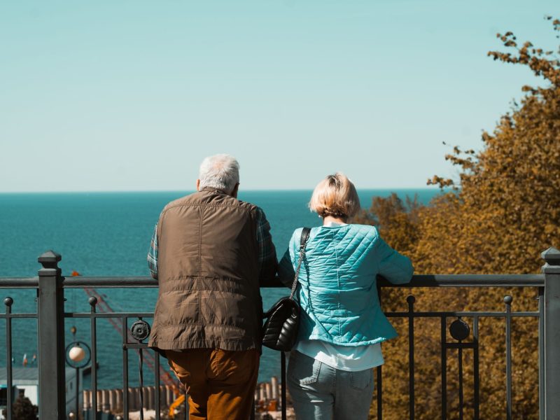 An older couple enjoys a serene view of the ocean while leaning on a railing, highlighting the importance of comfort in travel.