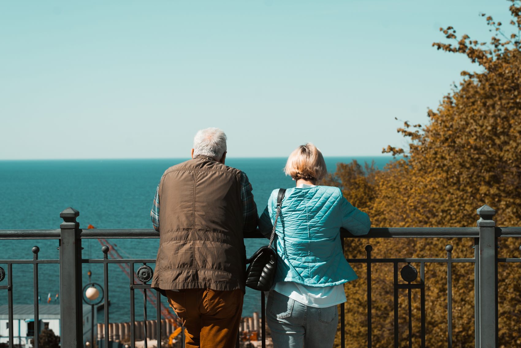 An older couple enjoys a serene view of the ocean while leaning on a railing, highlighting the importance of comfort in travel.