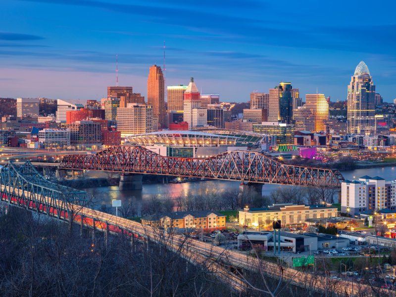 Cincinnati skyline at dusk featuring bridges, waterfront, and illuminated buildings showcasing the city's vibrant atmosphere.