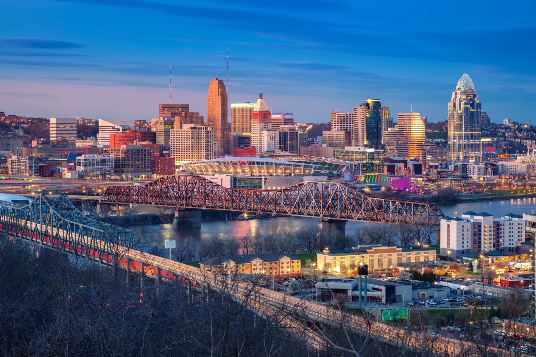 Cincinnati skyline at dusk featuring bridges, waterfront, and illuminated buildings showcasing the city's vibrant atmosphere.