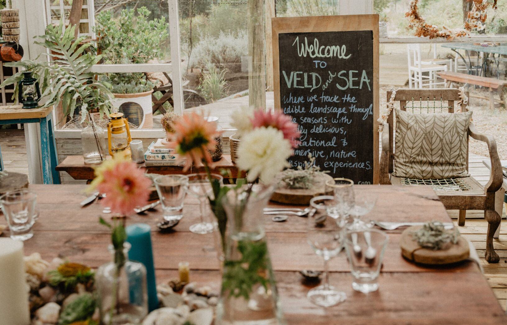 Decorated table with flowers and glassware, featuring a chalkboard sign welcoming guests to Veld and Sea in South Africa.