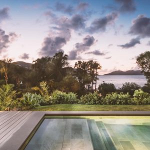 Luxury villa pool terrace overlooking lush greenery and tranquil sea at sunset, ideal for festive family gatherings.