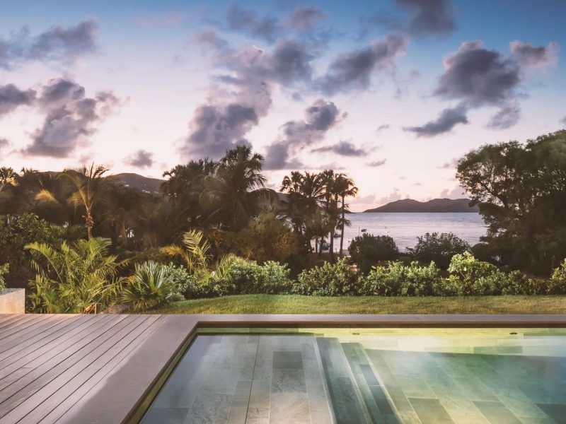 Luxury villa pool terrace overlooking lush greenery and tranquil sea at sunset, ideal for festive family gatherings.