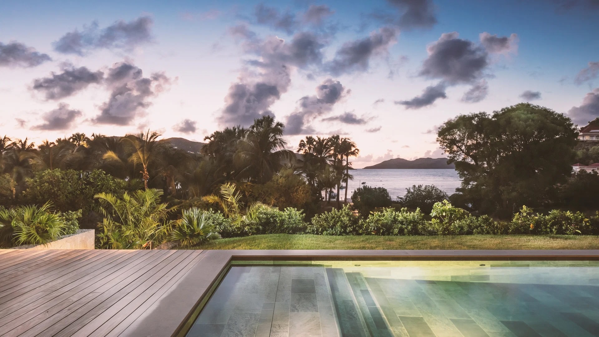 Luxury villa pool terrace overlooking lush greenery and tranquil sea at sunset, ideal for festive family gatherings.