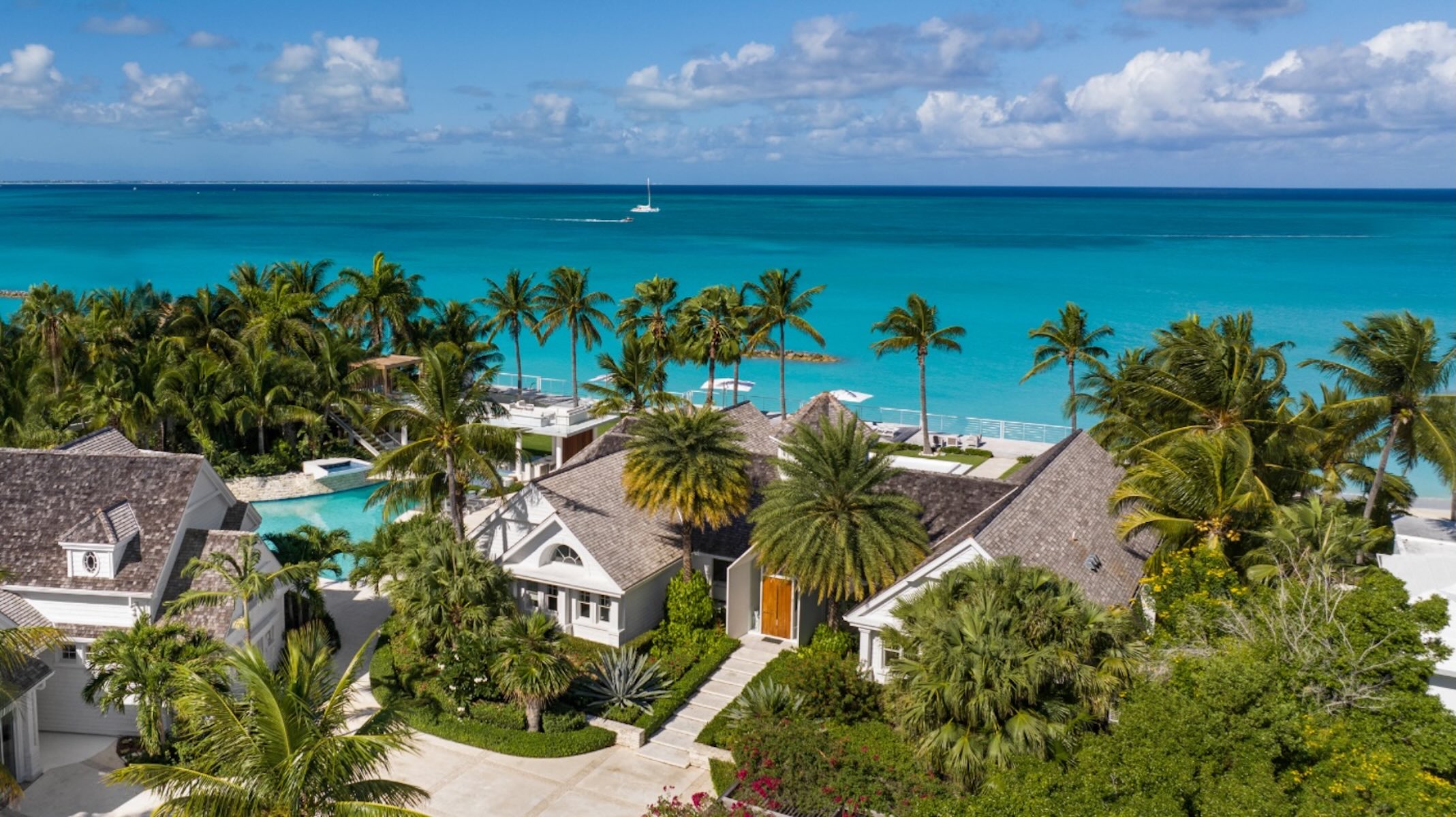 Luxurious beachfront property surrounded by palm trees and a clear turquoise sea, ideal for holiday retreats.