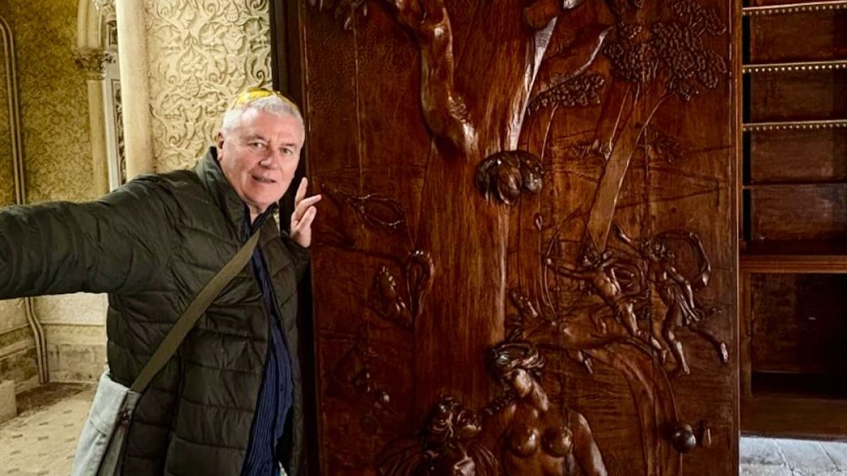 Person posing beside a detailed wooden relief carving of a tree and figures in an ornate interior space in Lisbon.