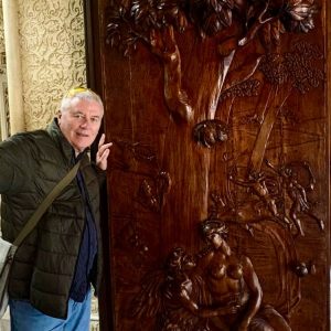 Person posing beside a detailed wooden relief carving of a tree and figures in an ornate interior space in Lisbon.