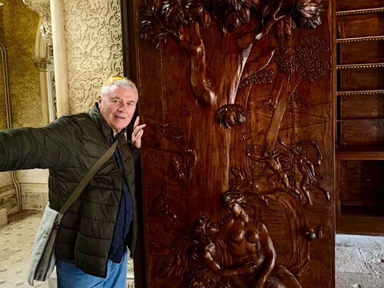 Person posing beside a detailed wooden relief carving of a tree and figures in an ornate interior space in Lisbon.