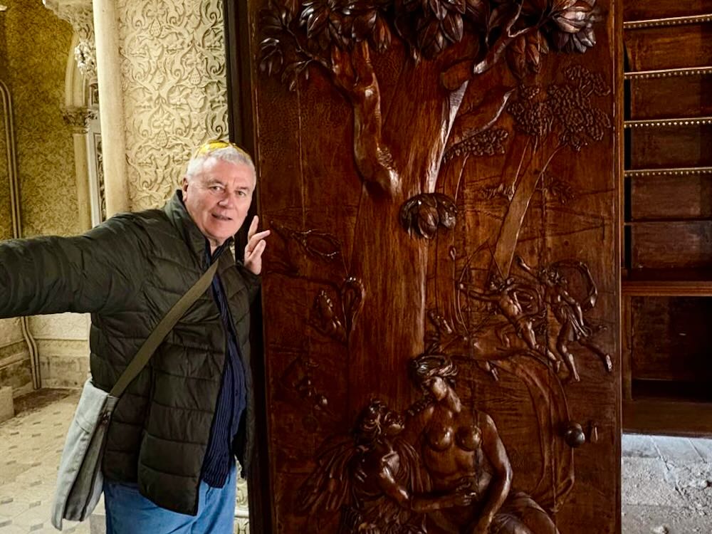 Person posing beside a detailed wooden relief carving of a tree and figures in an ornate interior space in Lisbon.