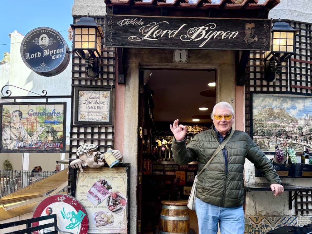 A man with sunglasses poses outside the Lord Byron café, showcasing its charming entrance and vibrant signage.